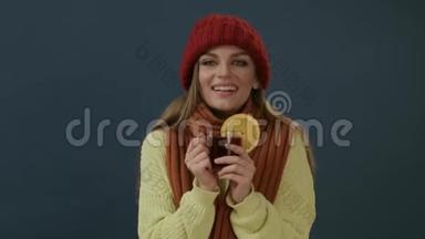 戴着围巾，戴着帽子，喝着热茶，喝着橘红色的酒的漂亮年轻女子